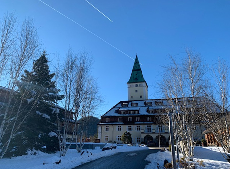 Schloss Elmau, der Tagungsort des G7-Gipfels im Januar 2022. Dargestellt ist die schneebedeckte Zufahrt zum Haupteingang bei blauem Himmel und Sonnenschein.