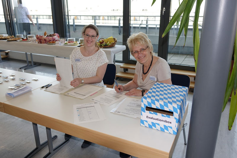 Zwei Mitarbeiterinnen der Bayerischen Gesundheitsagentur empfangen die Stipendiatinnen und Stipendiaten an der Anmeldung zum 5. Stipendiatenseminar