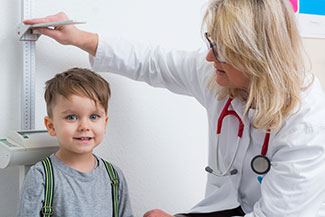 Das Bild zeigt eine blonde Frau im weißen Kittel, di bei einem kleinen Jungen die Körpergröße mißt.