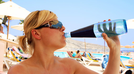 Frau am Strand trinkt Wasser