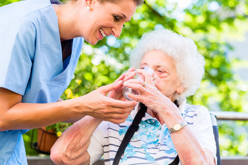 Das Bild zeigt eine Pflegerin, die einer Seniorin zu trinken gibt