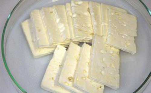 Original oder Fälschung? Die Abbildung zeigt mehrere kleine Scheiben eines weißen Käses ohne Rinde. Der Käseteig ist bröckelig und besitzt die Lochung, die für in Salzlake gereifte Käse wie Feta-Käse typisch ist. Um was für ein Erzeugnis es sich aber tatsächlich handelt, ist für den Verbraucher nicht unbedingt erkennbar.