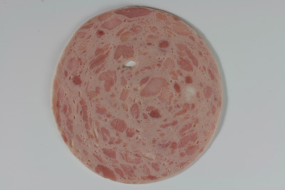 Schinkenwurst: Das Foto zeigt eine Scheibe Schinkenwurst. In einer fein zerkleinerten Masse („Brät“) befinden sich bis etwa erbsengroße Muskelfleischstückchen eingebettet.