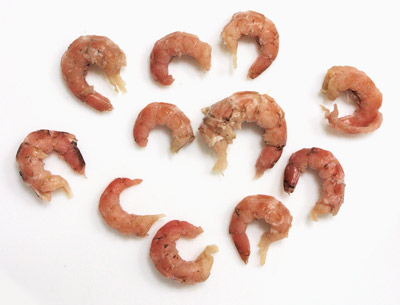 Das Foto zeigt das Fleisch von elf Nordseegarnelen. Es handelt sich um das Fleisch aus den Garnelenschwänzen. Die rötlichen Schwänze sind gekrümmt und laufen an einem Ende spitz zu.
