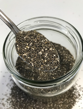 Das Bild zeigt ganze Chiasamen auf einem Edelstahllöffel über einem geöffneten Vorratsglas