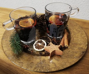 zwei Glastassen mit Glühwein auf einem goldenen Teller mit weihnachtlicher Dekoration