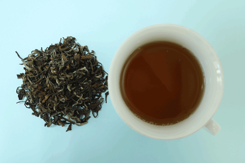 farbiges Bild eines zu bereiteten Ooloong-Tees und ein Haufen an Teeblättern  