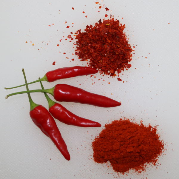 Vier frische, rote Chilischoten, und je ein Häufchen Chiliflocken und Chilipulver