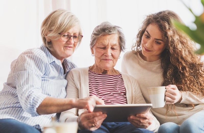 Drei Frauen unterschiedlicher Generationen schauen gemeinsam auf ein Tablet