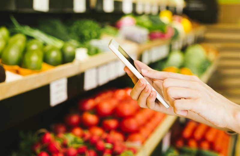 Mensch mit Handy steht im Supermarkt.
