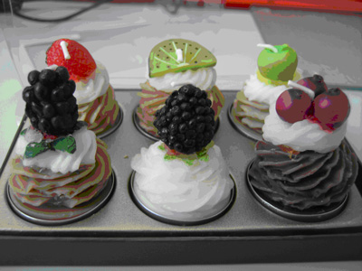 Die Abbildung zeigt eine Packung mit sechs Kerzen in Form von Sahne- oder Cremetörtchen, die mit Fruchtstücken dekoriert sind.