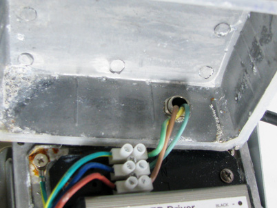 In Abbildung sind als Mangel die fehlende Zugentlastung der Netzleitung und der fehlender Anschluss des Schutzleiters am berührbaren Metalldeckel erkennbar.
